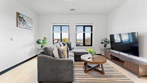 A modern living room with a grey sofa, a round coffee table, and a large flat-screen TV. - Luxury 2bd/2ba near Boston sly2 (Everett)