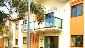 Um edifício de apartamentos moderno com varanda, um pequeno espaço de pátio com uma cadeira e um jardim bem cuidado.