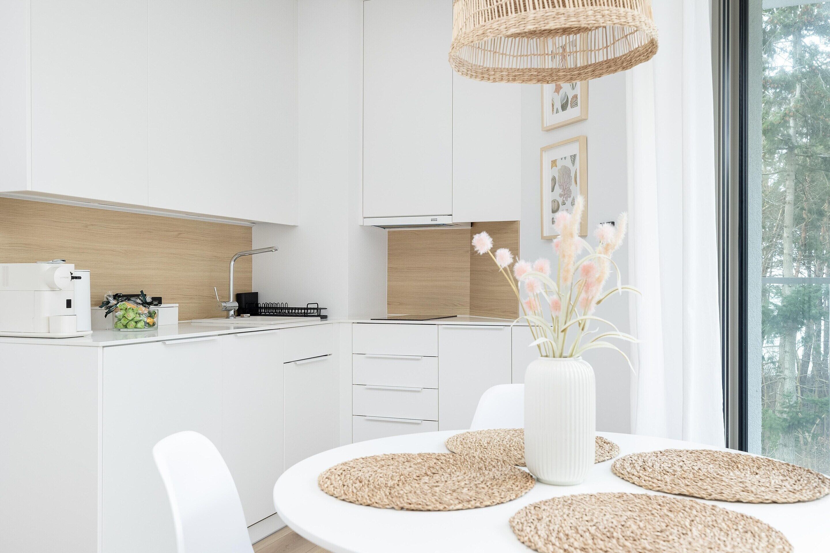 Cocina moderna con armarios blancos, protector contra salpicaduras de madera y un amplio ventanal con vistas a árboles.