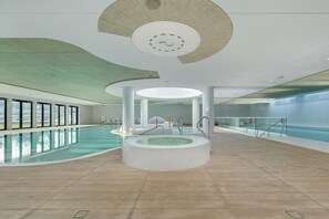 Piscina interna com uma banheira de hidromassagem central, grandes janelas e um design moderno no teto.