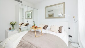 Een moderne slaapkamer met een groot bed, nachtkastjes, een bedlampje, een spiegel en een raam met gordijnen.
