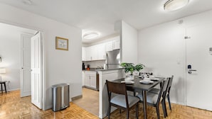 A modern kitchen with white cabinets, a stainless steel refrigerator, and a dining area with a table set for two. - Nice 2bd/1.5ba Next to BU 7qn5 (Boston)