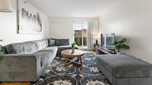 A modern living room with a grey sectional sofa, a round coffee table, and a patterned rug. - Nice 2bd/1.5ba Next to BU 7qn5 (Boston)