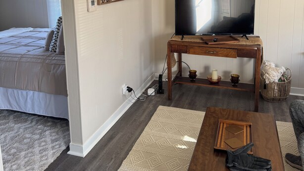 Una sala de estar con una cama, un televisor sobre un mueble de madera, una mesa de centro y un ventilador de techo.