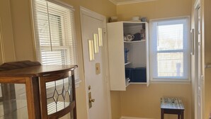 Una habitación con piso de madera, un aparador de vidrio, una puerta con ventanal y un estante empotrado con utensilios de cocina.