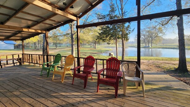 Eine überdachte Terrasse mit Holzboden und Metallgeländern, mit Blick auf einen See und Bäume.