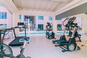 A gym with treadmills, elliptical machines, and a pool in the background.