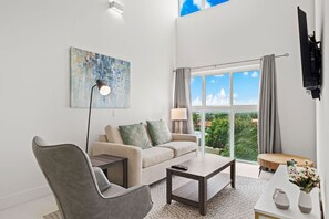 A modern living room with a sofa, armchair, coffee table, and artwork on the wall.