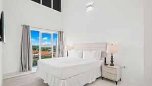 A bedroom with a bed, bedside tables, and a view through a window. - Charming 2BR Condo w/ Pool Access in Noord, Aruba (Noord)