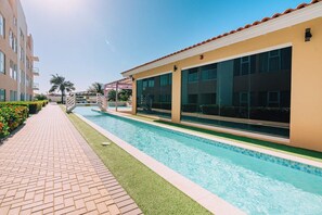 A swimming pool adjacent to a building with large windows and a tiled roof. - Charming 2BR Condo w/ Pool Access in Noord, Aruba (Noord)