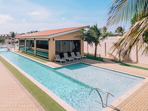 A swimming pool with lounge chairs and a covered area, surrounded by palm trees and a clear sky.