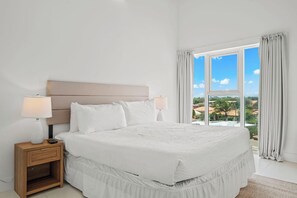 A bedroom with a large bed, two bedside tables, and a view of a landscape through a window. - Stunning 2-Bedroom Condo in Noord Aruba (Noord)