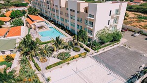 A hotel with a swimming pool, tennis court, and a parking area.