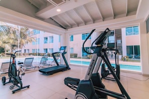 A gym with treadmills and an elliptical machine, large windows, and a view of a pool. - Stunning 2-Bedroom Condo in Noord Aruba (Noord)