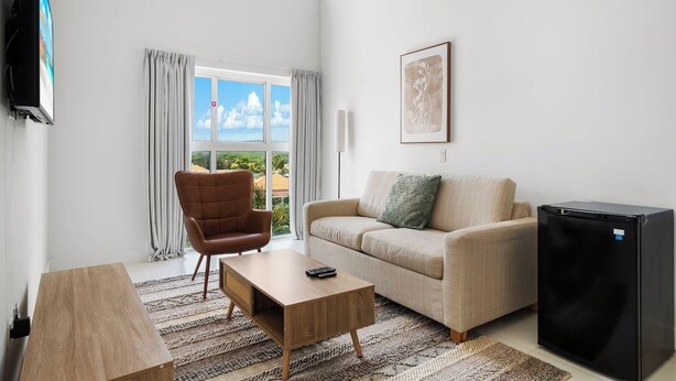 A modern living room with a sofa, armchair, coffee table, and a black refrigerator.