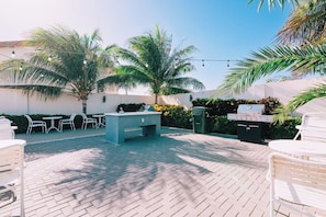 An outdoor patio area with a grill, seating, and palm trees. - Stunning 2-Bedroom Condo in Noord Aruba (Noord)