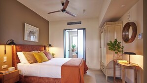 A well-lit bedroom with a bed, bedside lamps, a ceiling fan, a window, a plant, and a wooden cabinet. - Rastoni Acropolis (Athens)