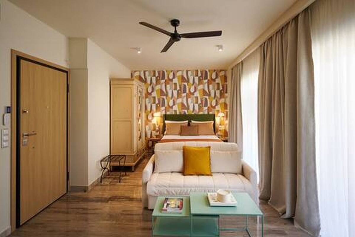 Ein Hotelzimmer mit einem Bett, einer Couch, einem Couchtisch, einem Deckenventilator und einer Wand mit geometrischem Muster.