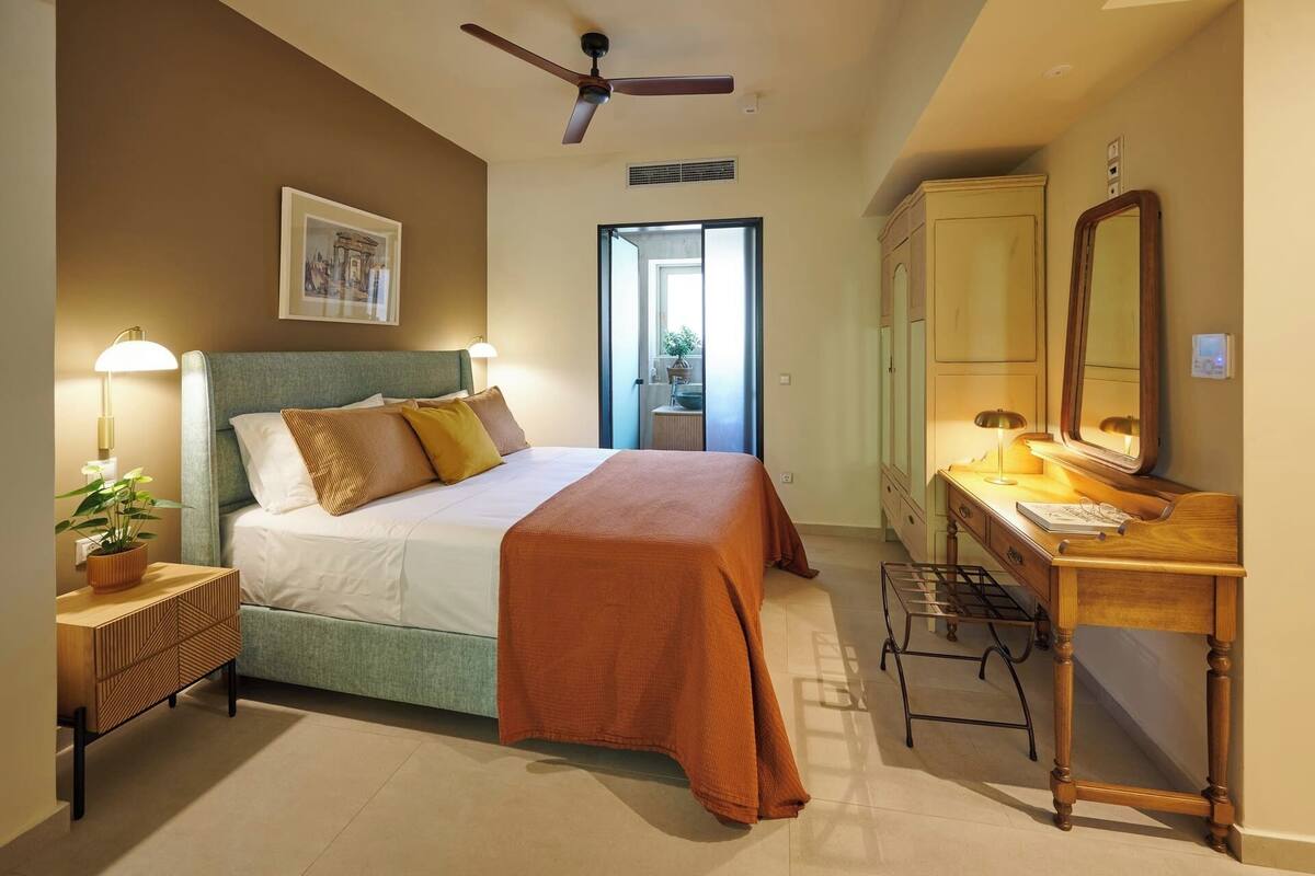 Ein Hotelzimmer mit Bett, Nachttisch, Lampe, Schminktisch, Spiegel und Deckenventilator.