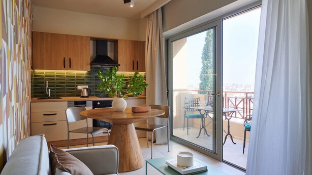A modern kitchen with wooden cabinets, a round wooden table, and a potted plant. - Rastoni Acropolis (Athens)