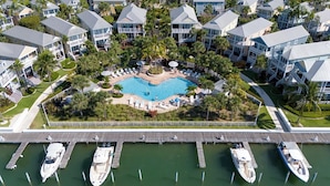 An aerial view of a resort with a central swimming pool surrounded by lounge chairs and palm trees, connected to the water by a dock with boats. - PRIME LOCATION Islamorada Anglers Reef Oceanview Private Beaches, Pool & Marina (Islamorada)