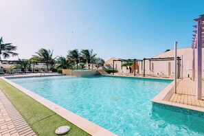 A swimming pool with a clear blue water, surrounded by palm trees and lounge chairs. - Noord Retreat: 2BR Condo with Pool Access - Aruba (Noord)