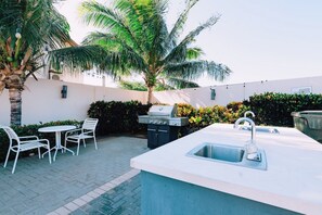 An outdoor kitchen area with a grill, a sink, and a dining set. - Third-Floor 2BR Condo w/ Lap Pool & Gym, Noord (Noord)