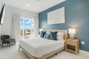 A bedroom with a bed, nightstands, a chair, and a window with curtains. - Noord Retreat: 2BR Condo with Pool Access - Aruba (Noord)