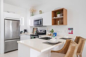 Eine moderne Küche mit einem Edelstahl-Kühlschrank, einer Mikrowelle und einem Einbauofen. Über der Arbeitsfläche befindet sich ein Holzboden mit Dekorationselementen.