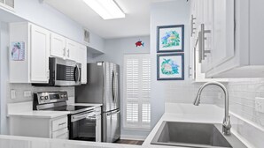 Una cucina moderna con mobili bianchi, un frigorifero in acciaio inossidabile, un microonde e un forno. Si notano due quadri appesi al muro e una decorazione a forma di pesce rosso sulla porta.