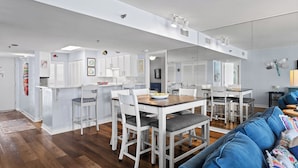 Una cucina moderna con mobili bianchi, un'area pranzo con sedie bianche e un divano blu nel soggiorno.