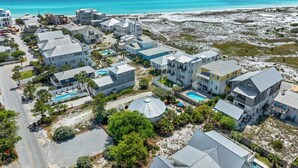 Et kystnære boligområde med flere huse, en swimmingpool og en strand i baggrunden.