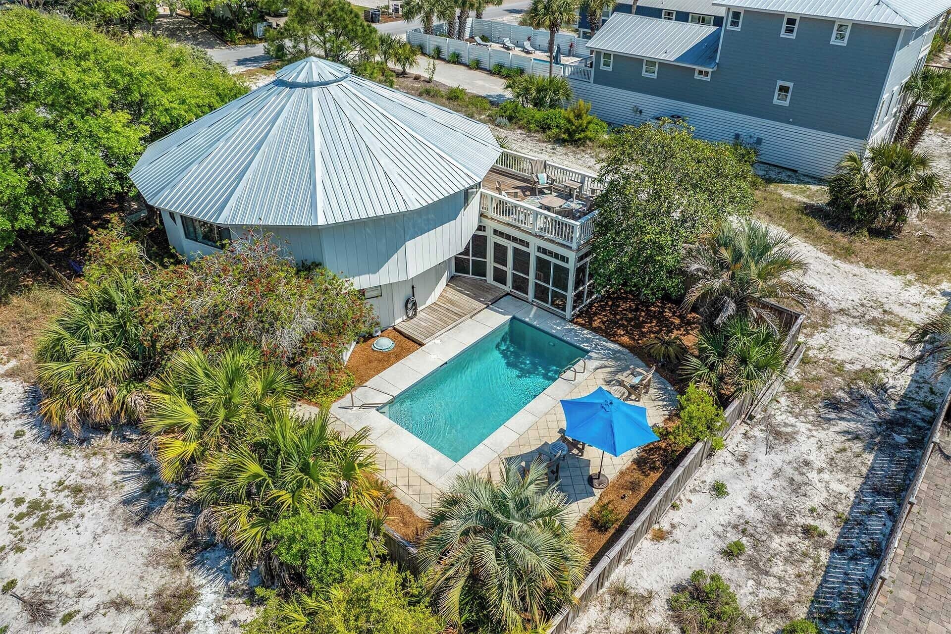 A large house with a swimming pool surrounded by tropical plants.