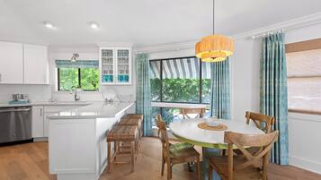 A kitchen with white cabinets, a large island, and a dining area with wooden chairs and a round table.