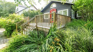 Een houten terras leidt naar een huis met een rode deur, omgeven door weelderige begroeiing.