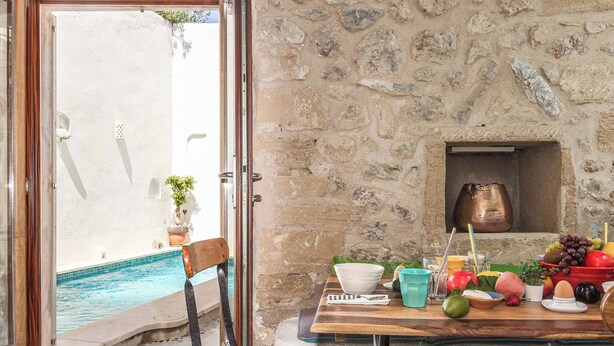 A dining area with a stone wall, a pool, and a table set with fruits and a copper pot.