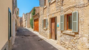 A narrow street lined with stone buildings, some with wooden shutters, and a clear blue sky.