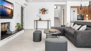 Un salon moderne avec un canapé gris, une petite table ronde et un téléviseur à écran plat fixé au mur.