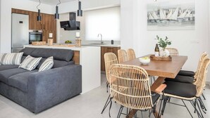 Un espace de vie moderne comprenant un canapé gris, des fauteuils en osier, une table à manger en bois et un coin cuisine avec des meubles en bois et un téléviseur à écran plat.