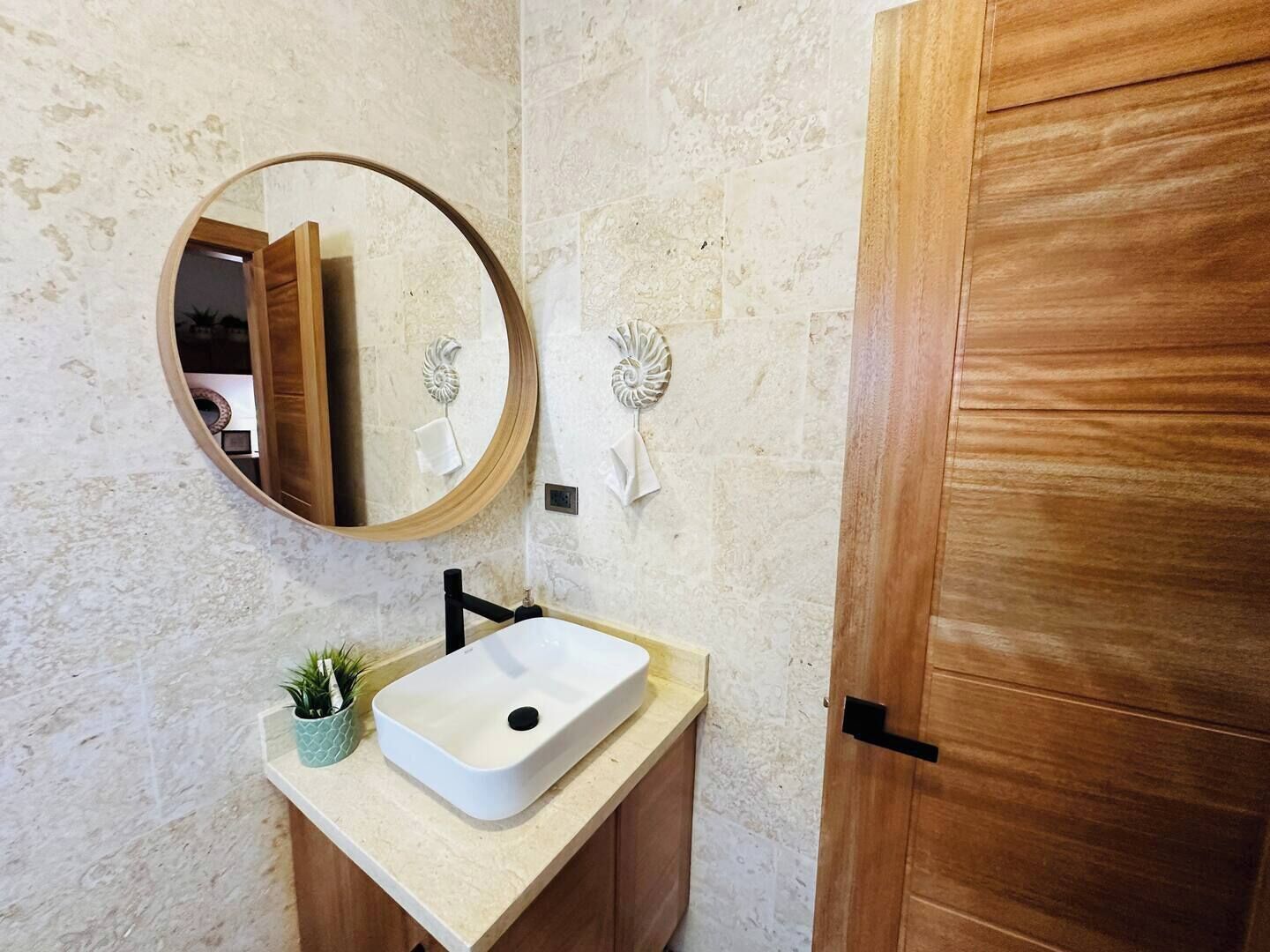 Ein Badezimmer mit Waschbecken, einem runden Spiegel und einer Holztür.