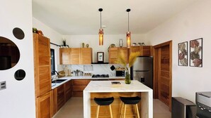 A modern kitchen with wooden cabinets, a marble countertop, two bar stools, and a built-in stove. - Coastal Luxe SOV: 3 Bed, 3.5 Bath, Sosúa Ocean Village (Sosúa)