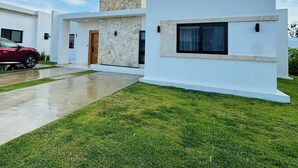 A modern two-story house with a stone facade, a red car parked in the driveway, and a well-maintained lawn. - Coastal Luxe SOV: 3 Bed, 3.5 Bath, Sosúa Ocean Village (Sosúa)