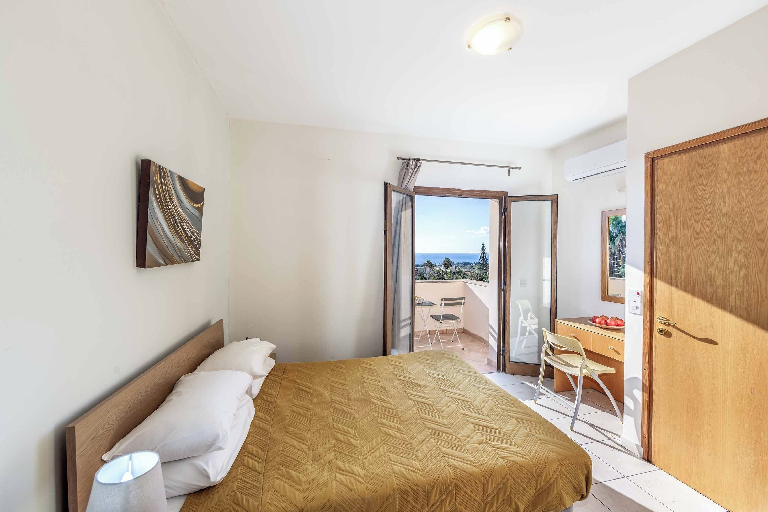Een slaapkamer met een bed, een bureau en een stoel. Er is een balkon met uitzicht.
