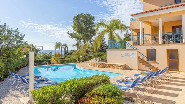 Un espace piscine avec des chaises longues, un bâtiment doté d’un balcon et une vue sur la mer.