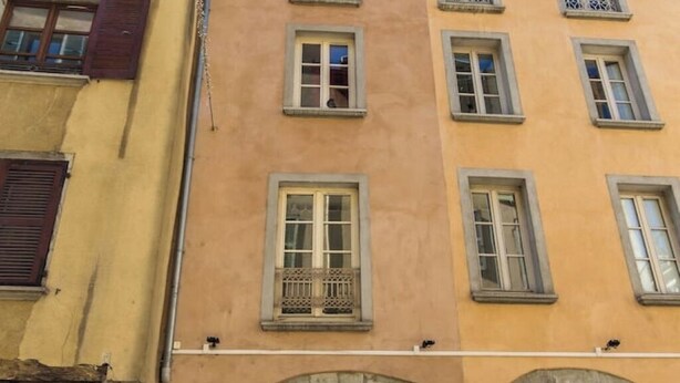 A multi-story building with a yellow facade, multiple windows with shutters, and a stone archway entrance. - T3 au vert sup downtown Grenoble (Grenoble)