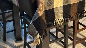 A dining area with a table covered by a quilt, surrounded by chairs.