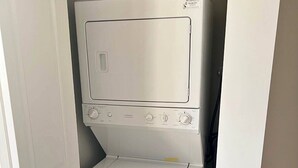 A compact, stainless steel washer and dryer unit in a small, enclosed space with a door.