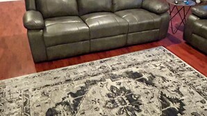 A living room with a dark leather sofa, a patterned rug, and a small coffee table.