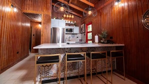 A kitchen with wooden walls, a central island with bar stools, a refrigerator, and a microwave. - Home with Pool & Pickleball Court near El Yunque (Palma Sola)