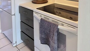 Une cuisine avec un réfrigérateur blanc, une cuisinière et un four à micro-ondes. Il y a des placards au-dessus de la cuisinière et une machine à café sur le plan de travail.